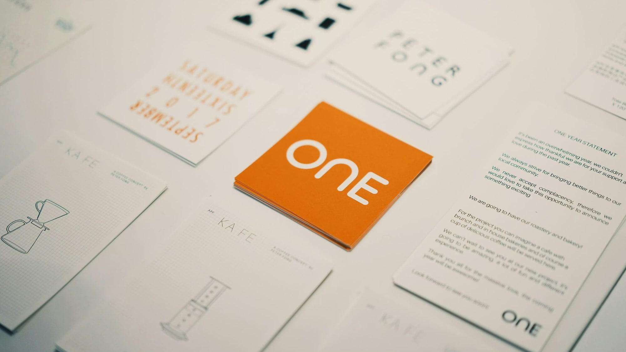 A brand identity laid out in print: business cards, letterheads and an orange logo card on a pale surface.