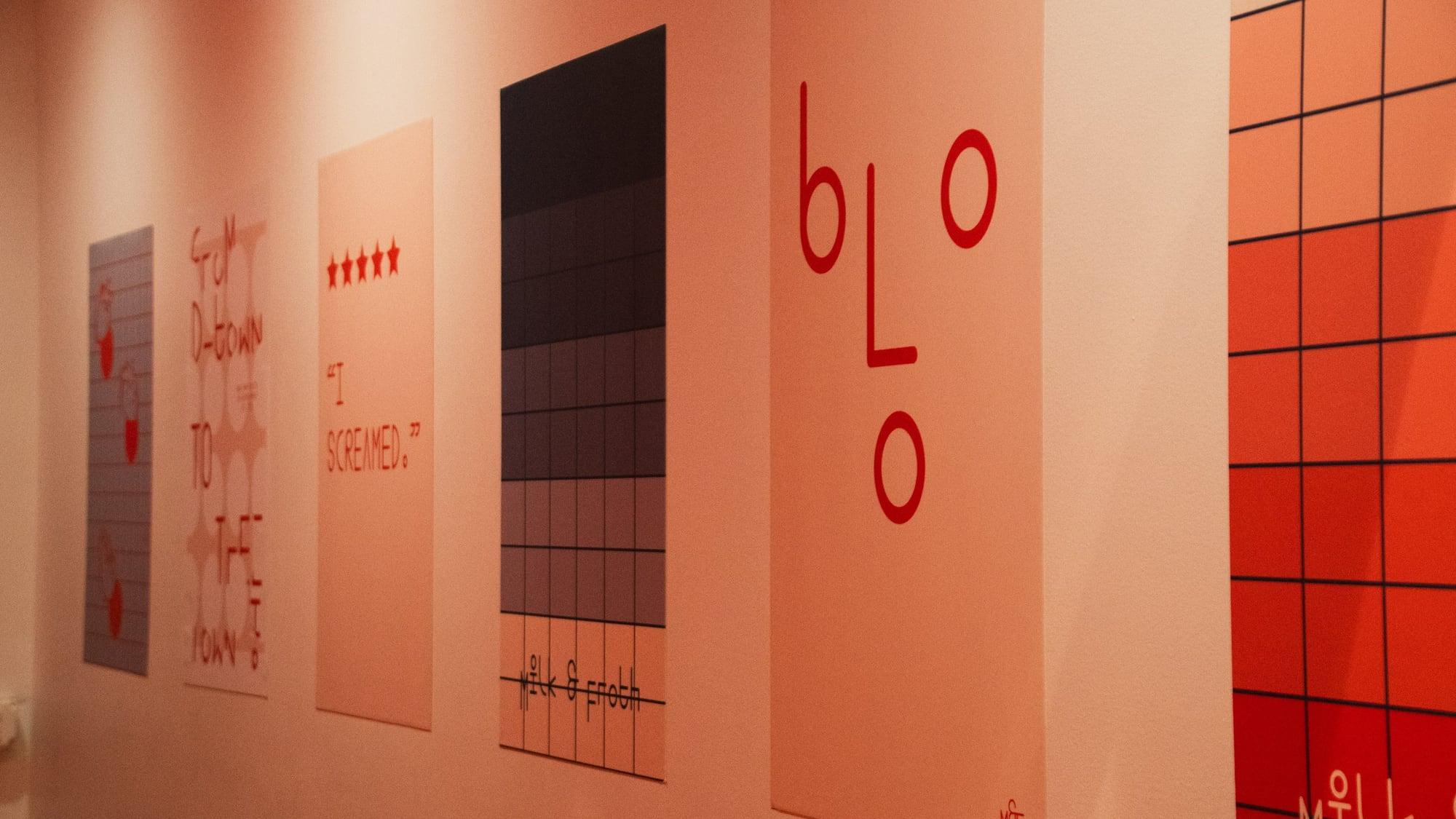 Printed posters hung in a row on a warm painted wall, each one a different typographic layout.